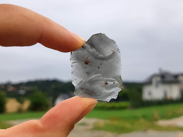 A fragment of a gray mineral held up to the light by two fingers. It is so thin that it almost shines through